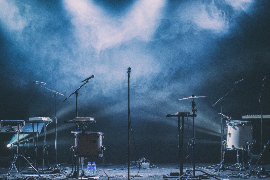 Empty stage with mics, drums, and cables under blue concert lights