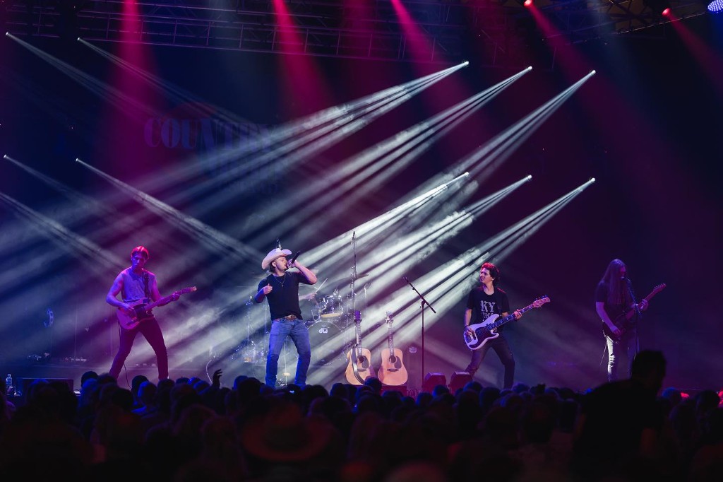 Country band performing live under bright stage lights with a full crowd